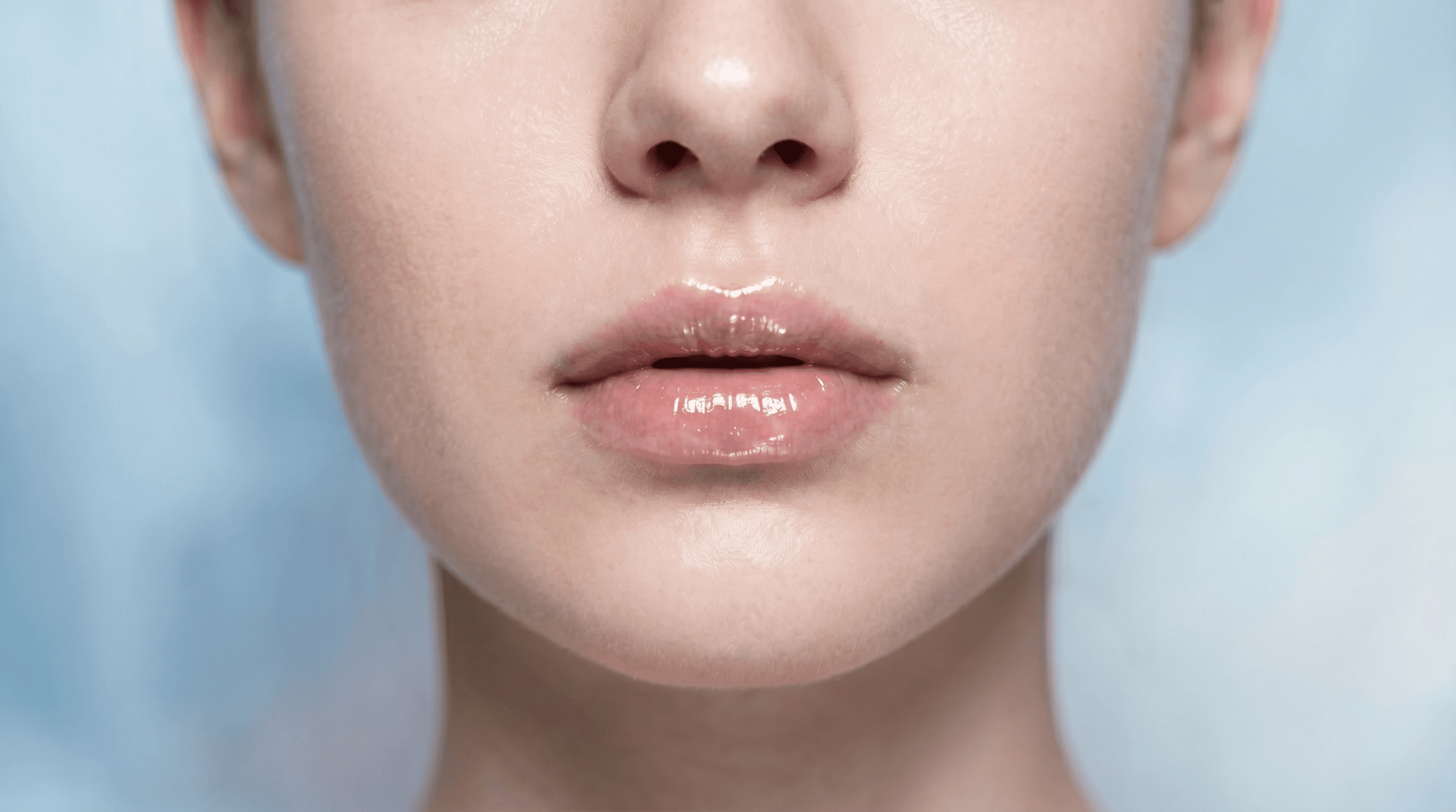 A close-up editorial shot of perfectly hydrated, plump lips with a soft glossy finish, surrounded by premium lip treatment products on a marble surface